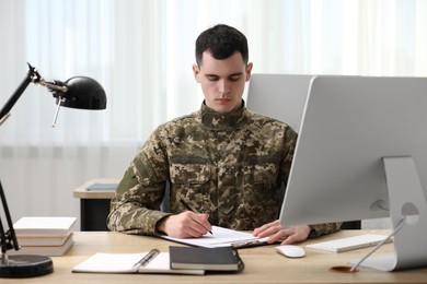 Photo of Military service. Young soldier working at wooden table in office