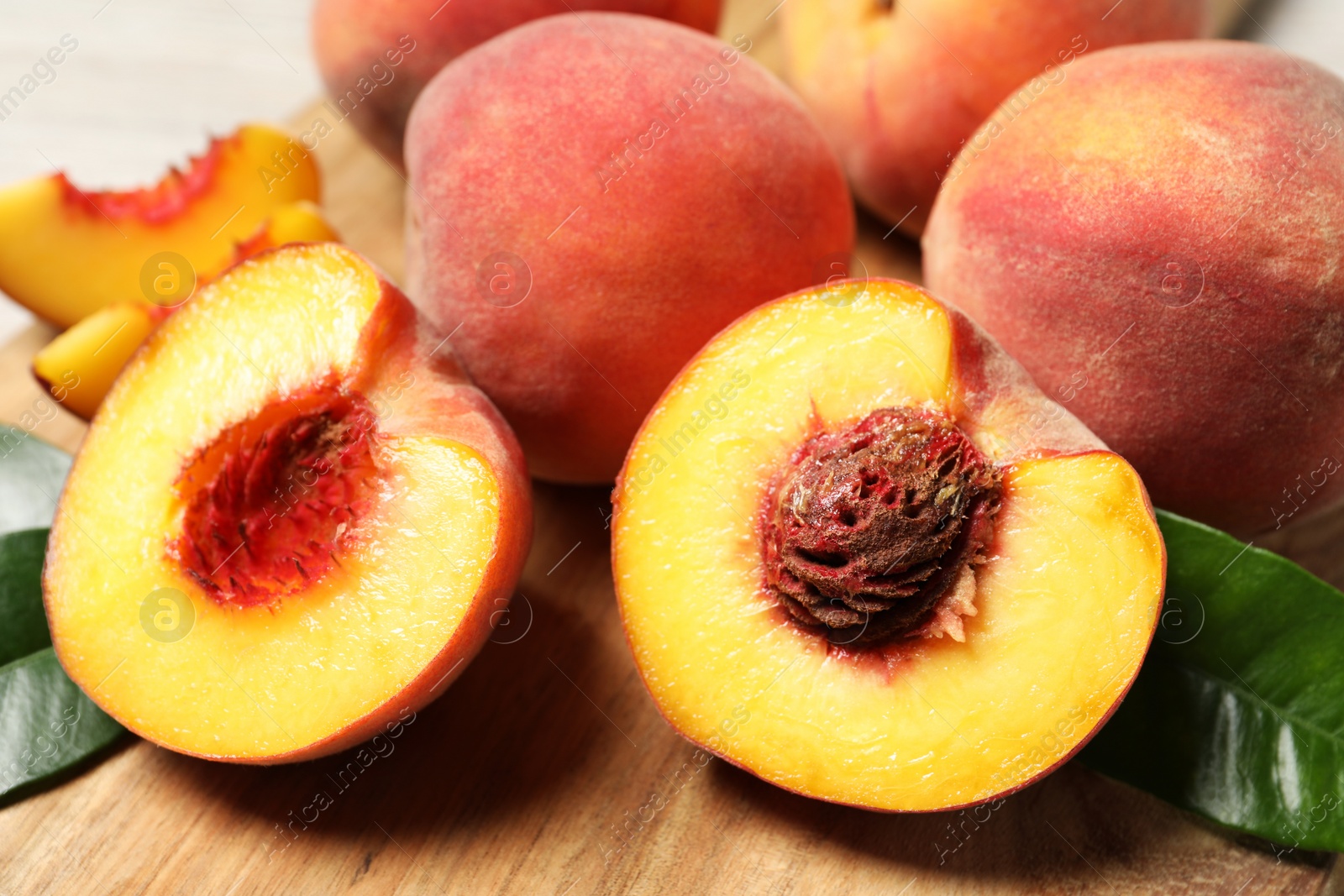 Photo of Cut and whole fresh ripe peaches on wooden board, closeup