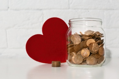 Photo of Donation jar with coins and red heart on table. Space for text