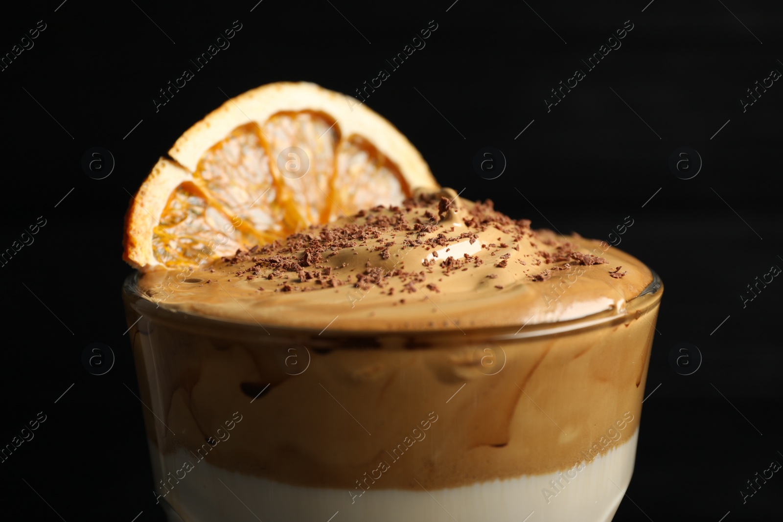 Photo of Glass of delicious dalgona coffee with dry orange and chocolate on black background, closeup