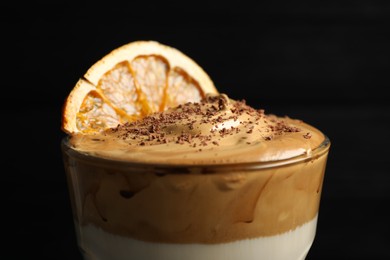 Glass of delicious dalgona coffee with dry orange and chocolate on black background, closeup