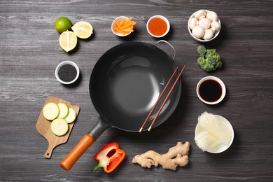 Photo of Empty iron wok and chopsticks surrounded by ingredients on dark grey wooden table, flat lay