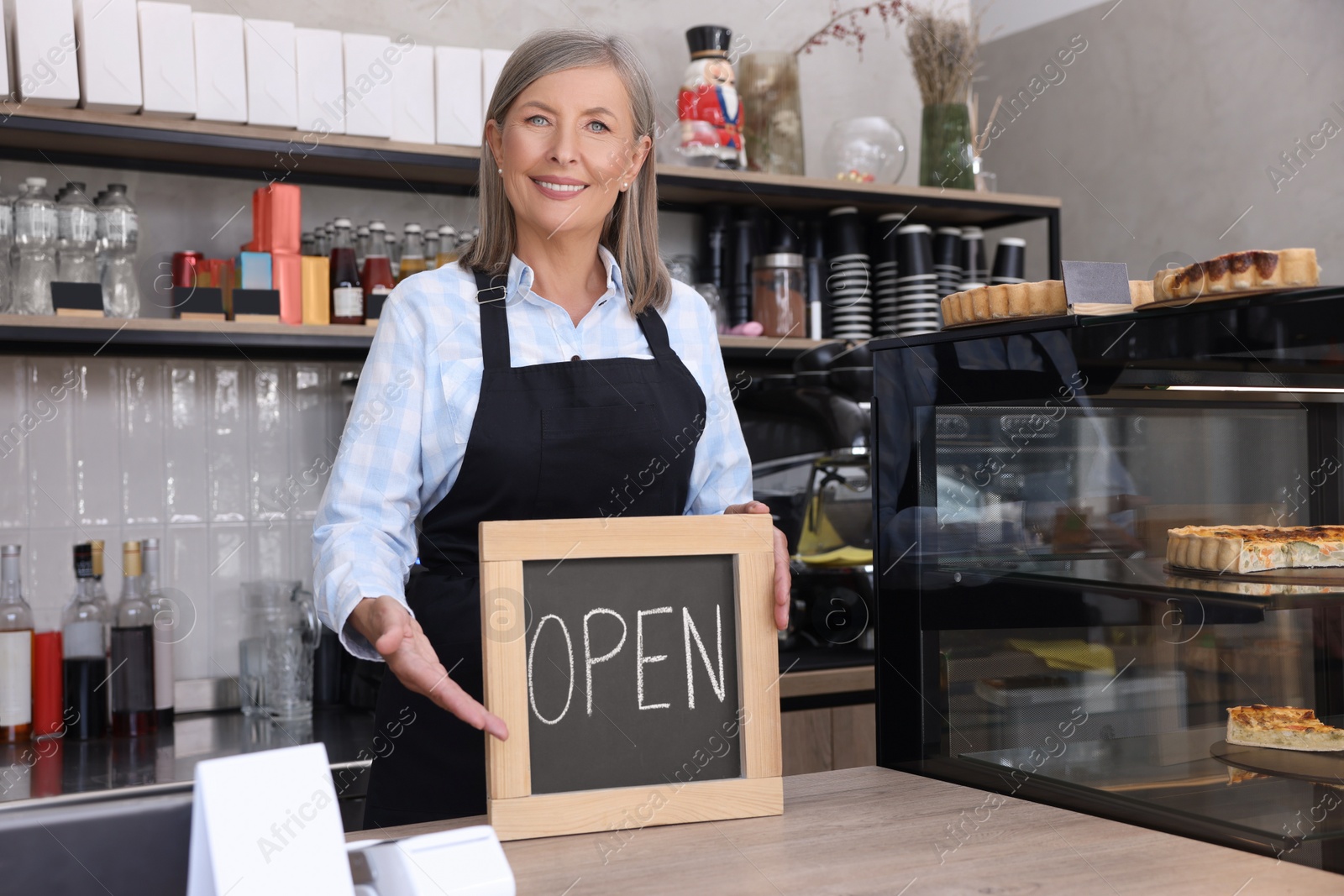 Photo of Happy business owner holding open sign at cashier desk in her cafe