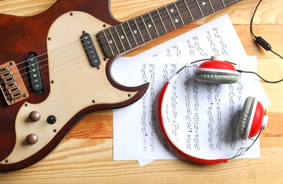 Modern electric guitar, headphones and music sheets on wooden background, top view