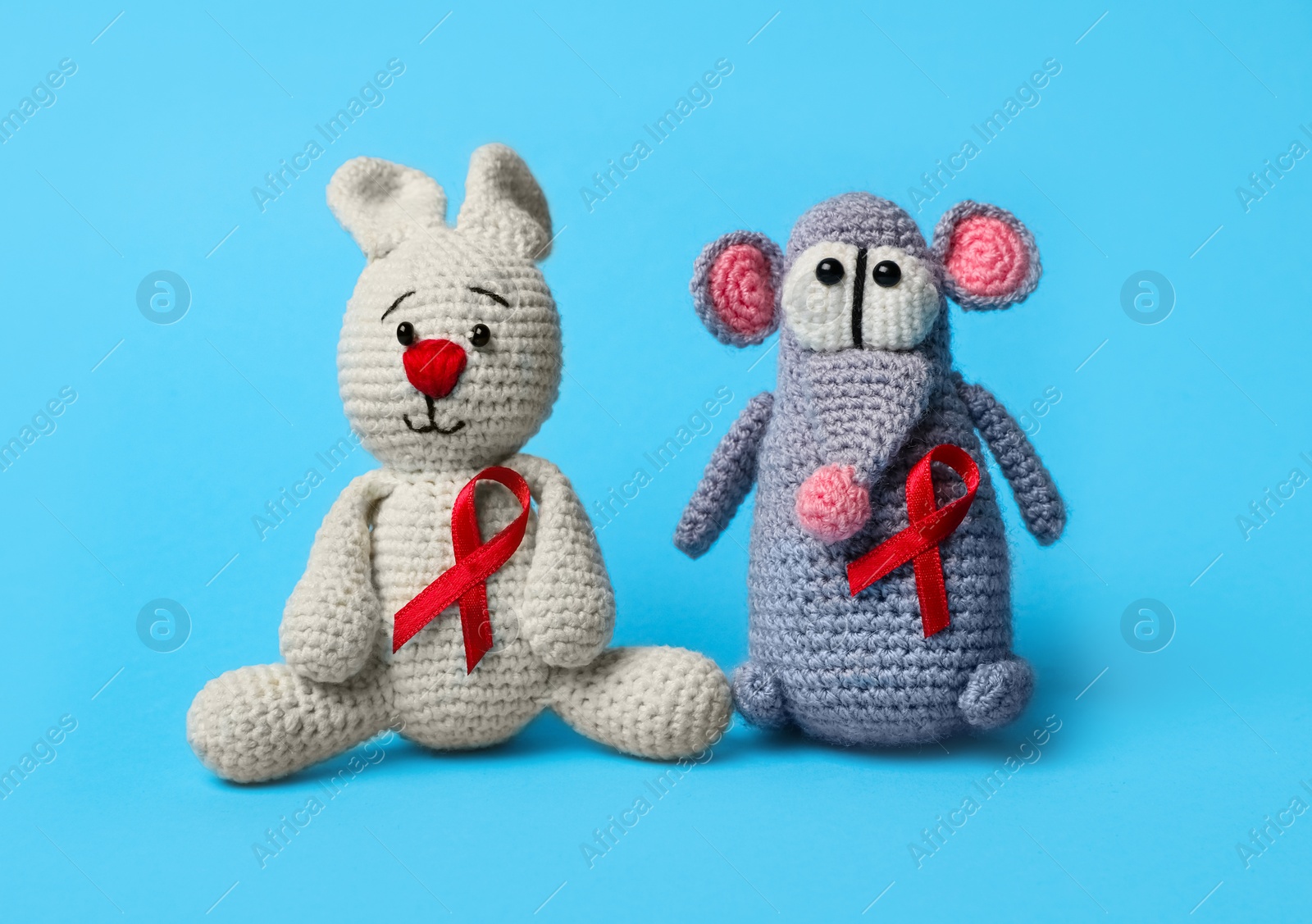 Photo of Cute knitted toys with red ribbons on blue background. AIDS disease awareness