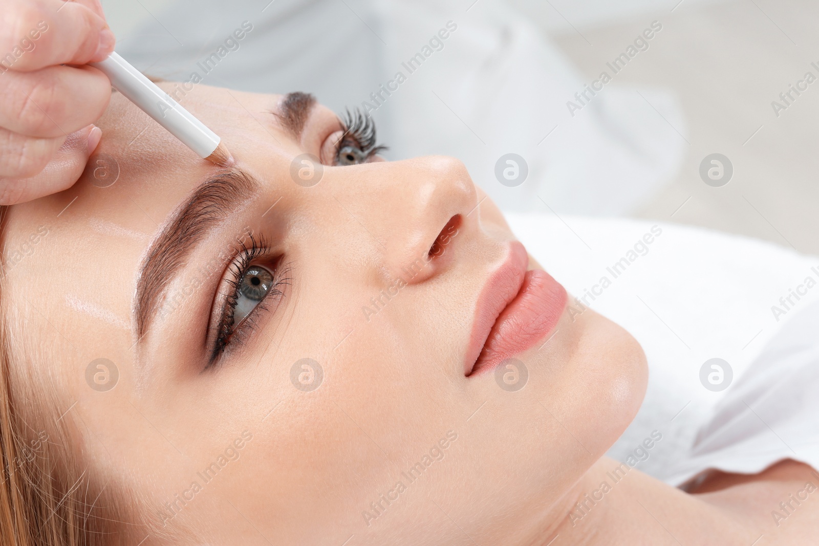 Photo of Cosmetologist preparing young woman for  eyebrow permanent makeup procedure, closeup