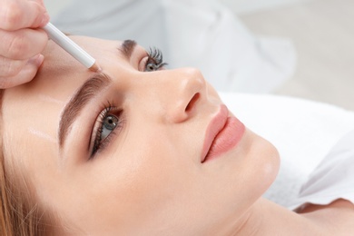 Photo of Cosmetologist preparing young woman for  eyebrow permanent makeup procedure, closeup