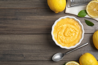 Delicious lemon curd in bowl on wooden table, flat lay. Space for text