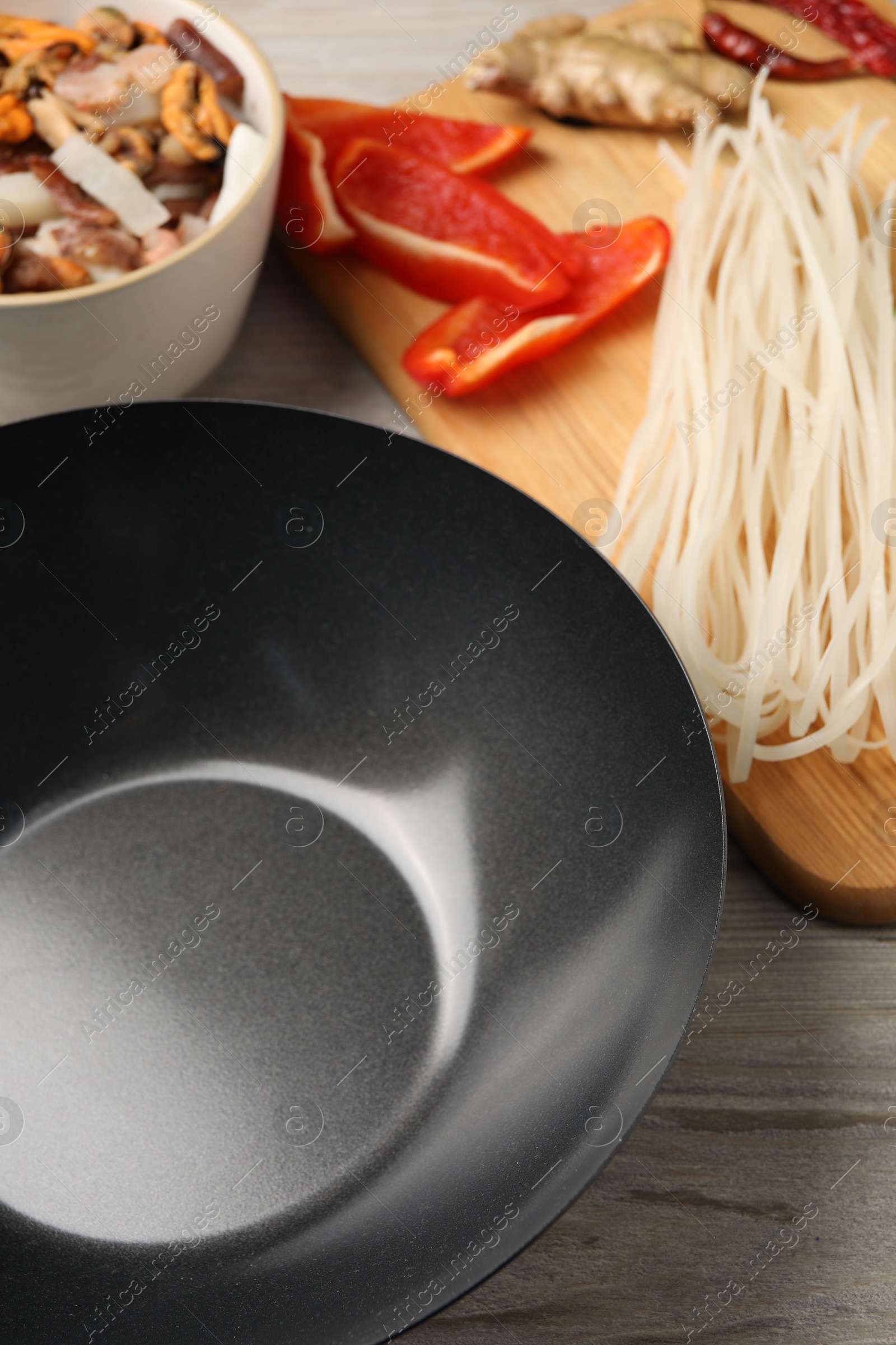 Photo of Black wok and products on light wooden table, closeup