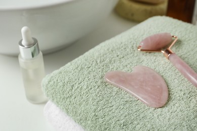 Rose quartz gua sha tool and natural face roller on towel in bathroom, closeup