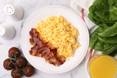 Photo of Delicious scrambled eggs with bacon served on white marble table, flat lay