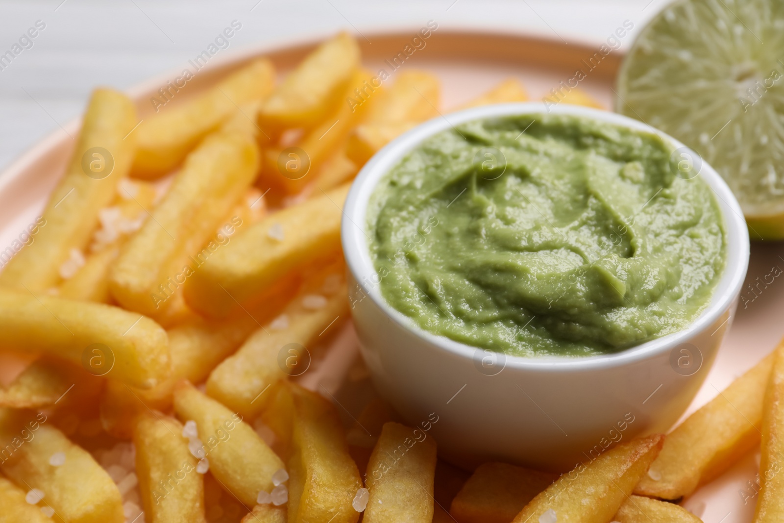 Photo of Plate with french fries, lime and avocado dip on white wooden table, closeup