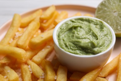Photo of Plate with french fries, lime and avocado dip on white wooden table, closeup
