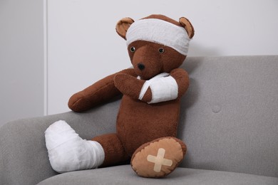 Photo of Toy bear with bandages sitting on sofa near light wall