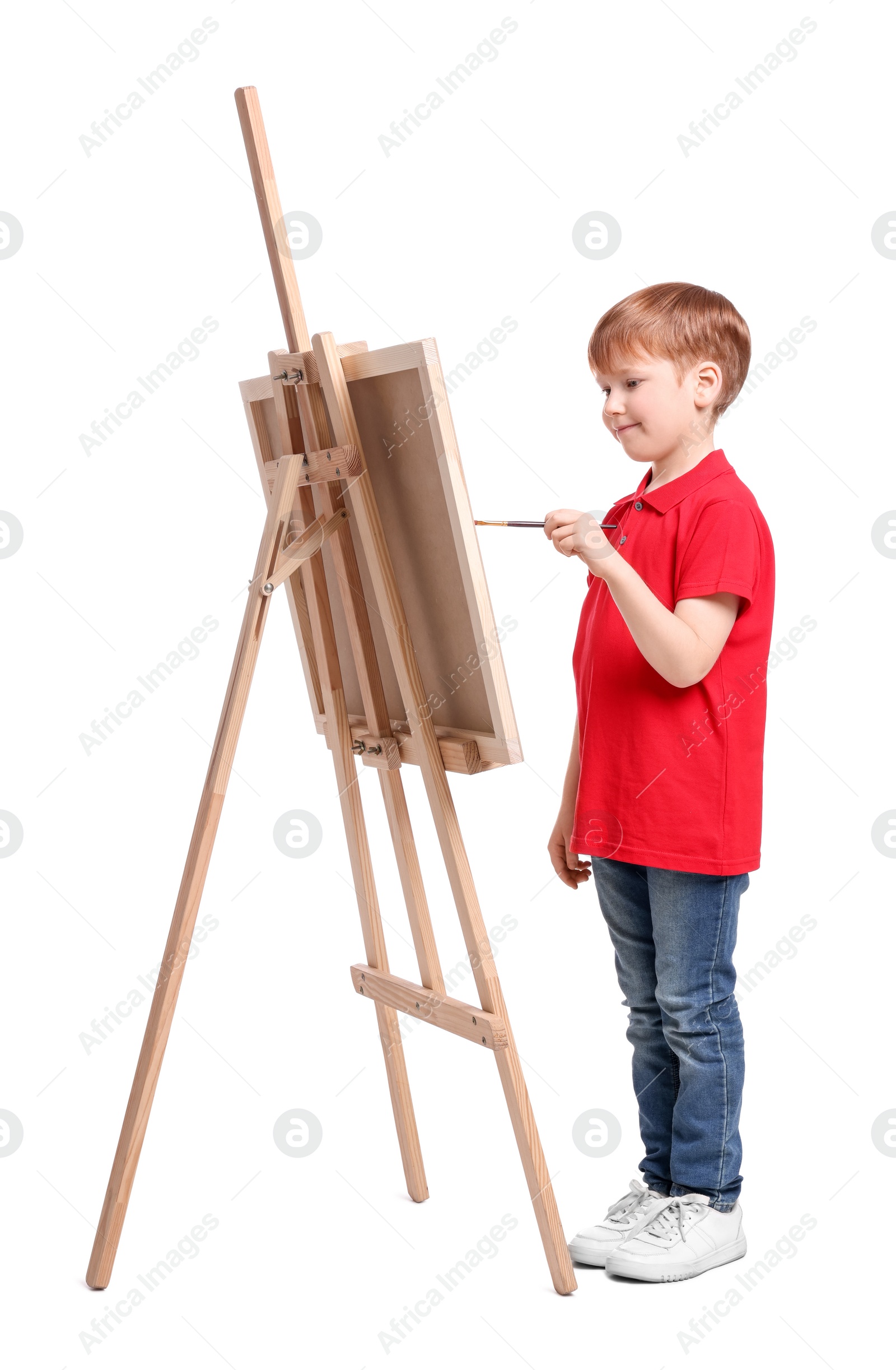 Photo of Little boy painting against white background. Using easel to hold canvas