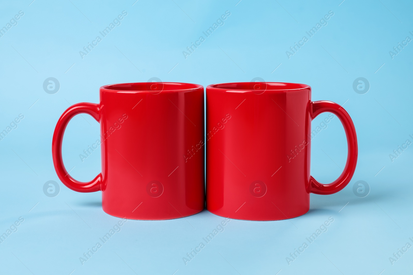 Photo of Two red ceramic mugs on light blue background