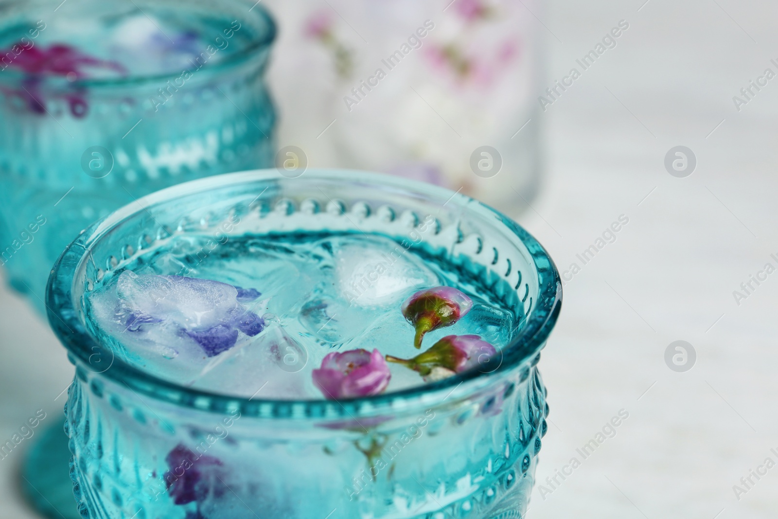 Photo of Glass with floral ice cubes and water on table, closeup. Space for text