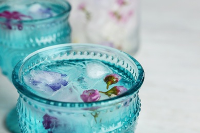 Photo of Glass with floral ice cubes and water on table, closeup. Space for text