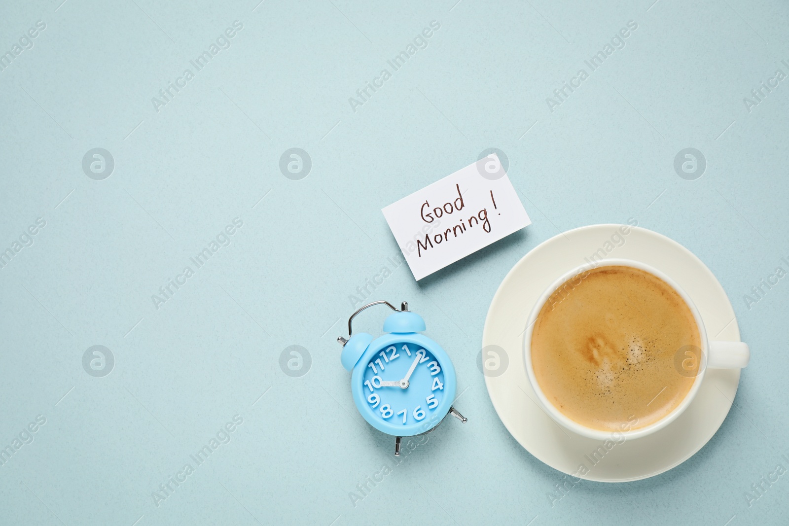 Photo of Delicious coffee, alarm clock and card with GOOD MORNING wish on light background, flat lay. Space for text