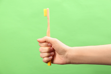 Photo of Woman holding bamboo toothbrush on green background, closeup