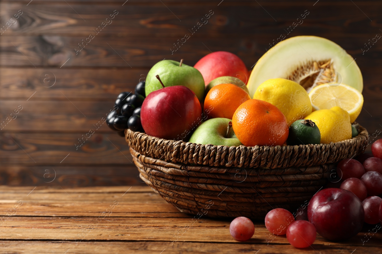 Photo of Different ripe fruits in wicker basket on wooden table, closeup. Space for text