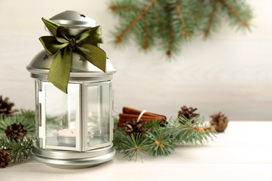 Photo of Christmas lantern with burning candle and fir tree branch on white wooden background