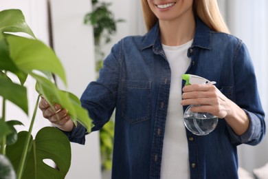 Woman spraying beautiful houseplants with water at home, closeup