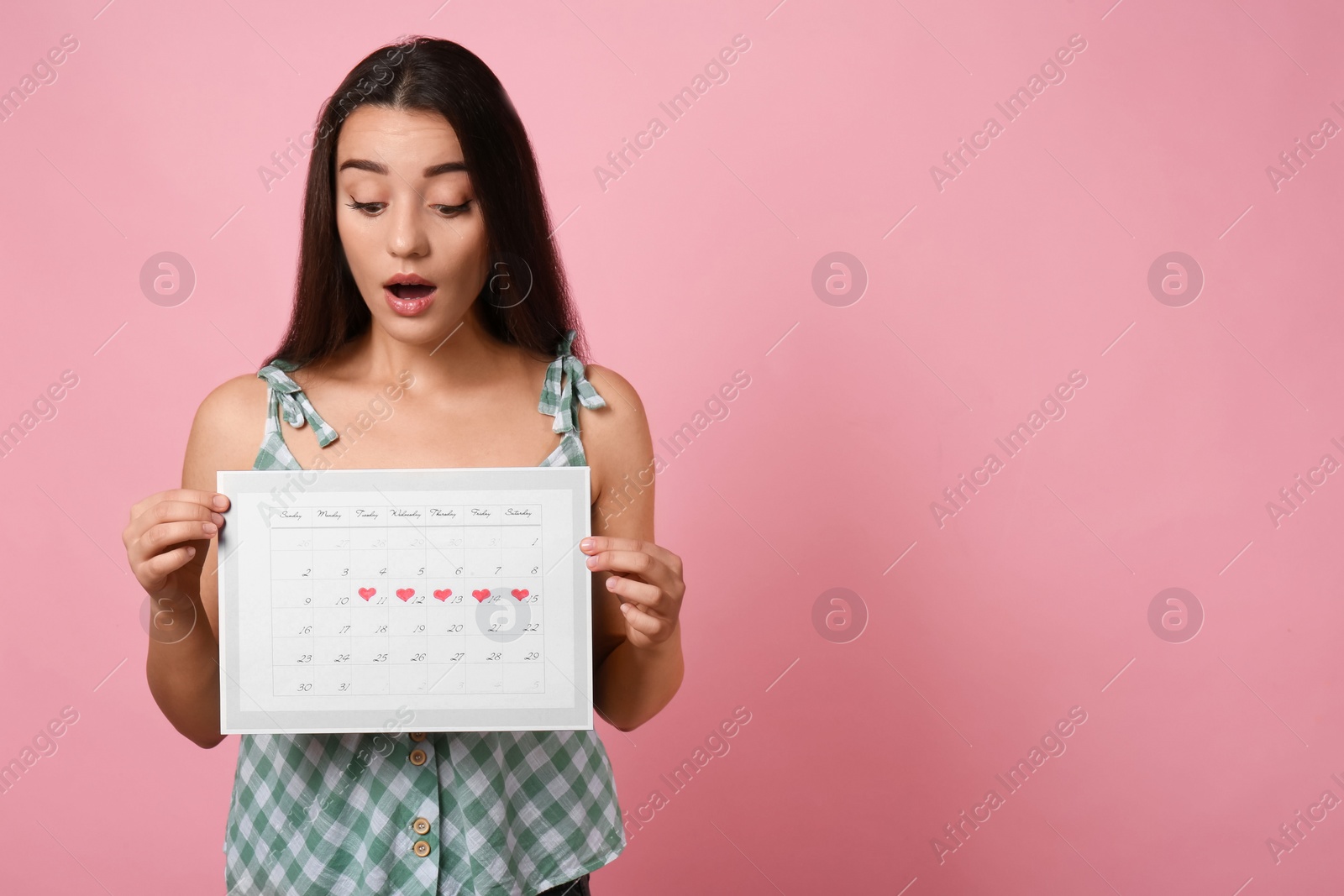 Photo of Young woman holding calendar with marked menstrual cycle days on pink background. Space for text