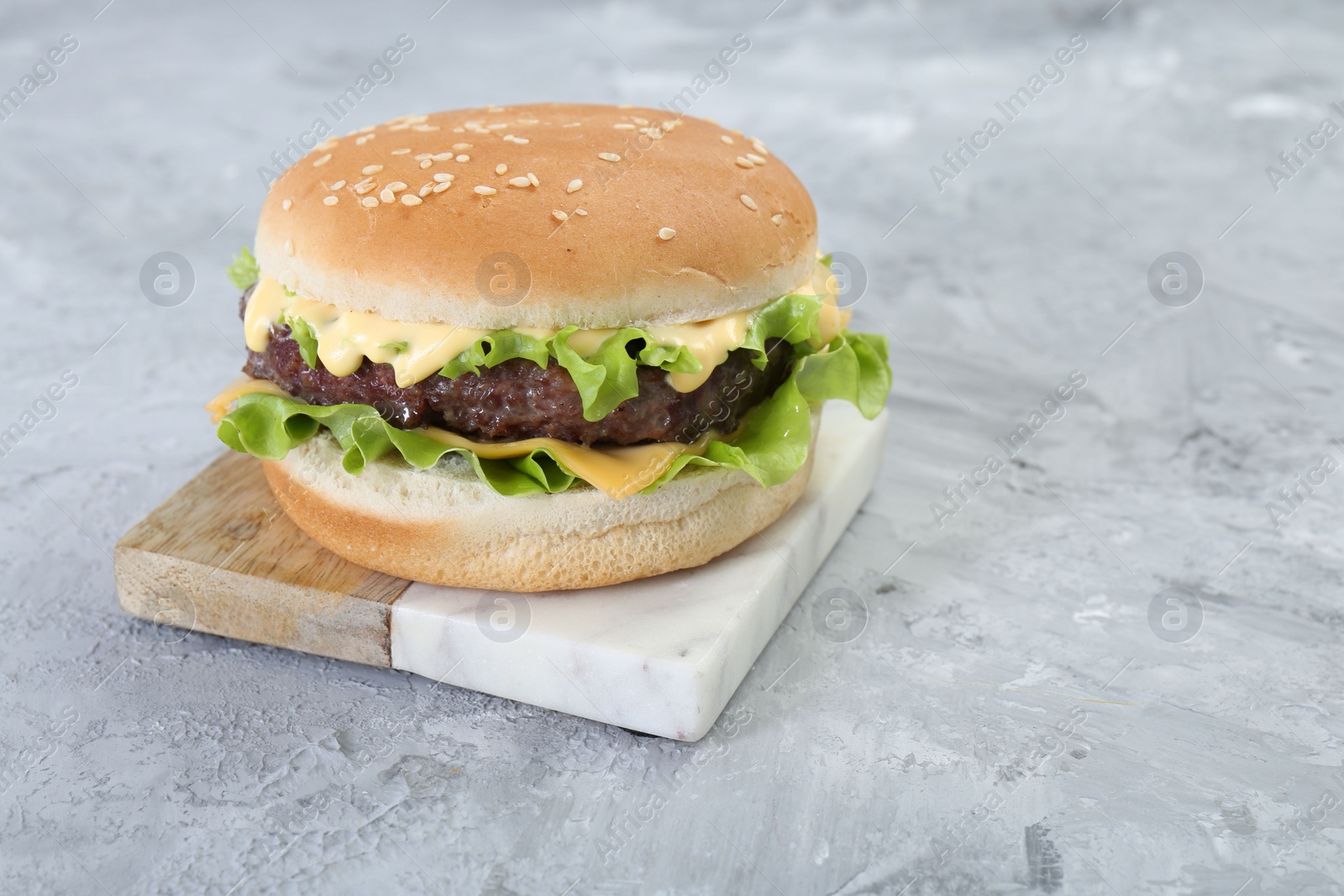 Photo of Delicious cheeseburger on grey textured table, closeup. Space for text