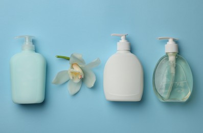 Bottles of liquid soap and flower on light blue background, flat lay