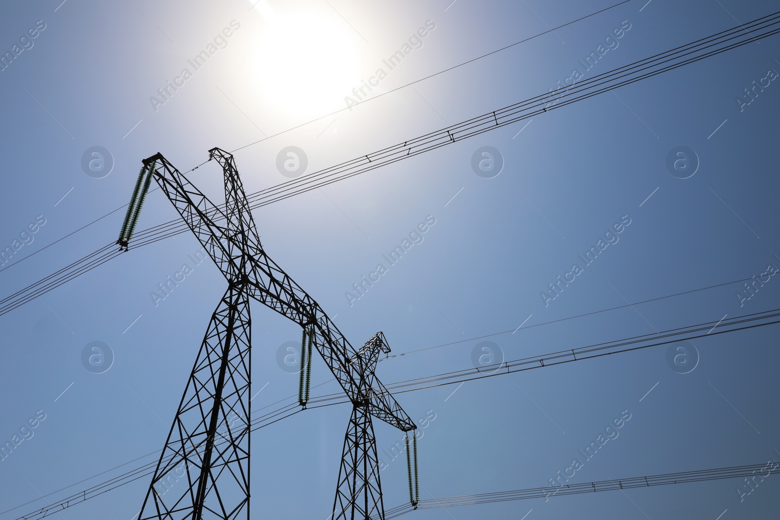 Photo of High voltage tower with electricity transmission power lines against blue sky, low angle view