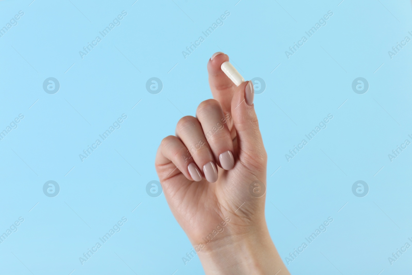 Photo of Woman holding vitamin capsule on light blue background, closeup. Health supplement