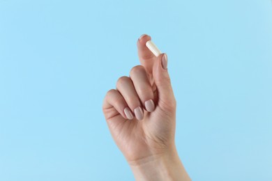 Photo of Woman holding vitamin capsule on light blue background, closeup. Health supplement