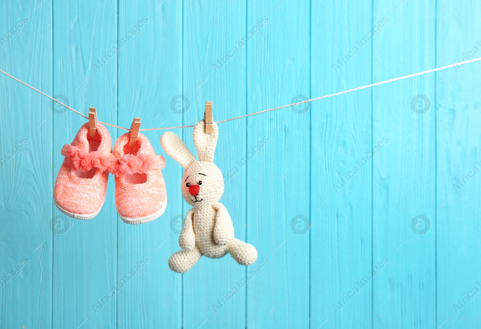 Photo of Baby shoes and toy bunny on laundry line against color wooden background, space for text. Child accessories