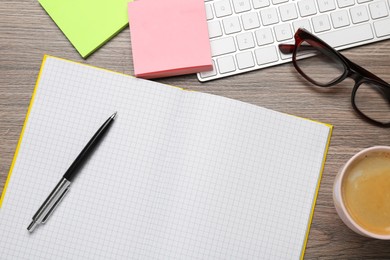 Photo of Blank notebook, cup of coffee and stationery on wooden table, flat lay. Space for text