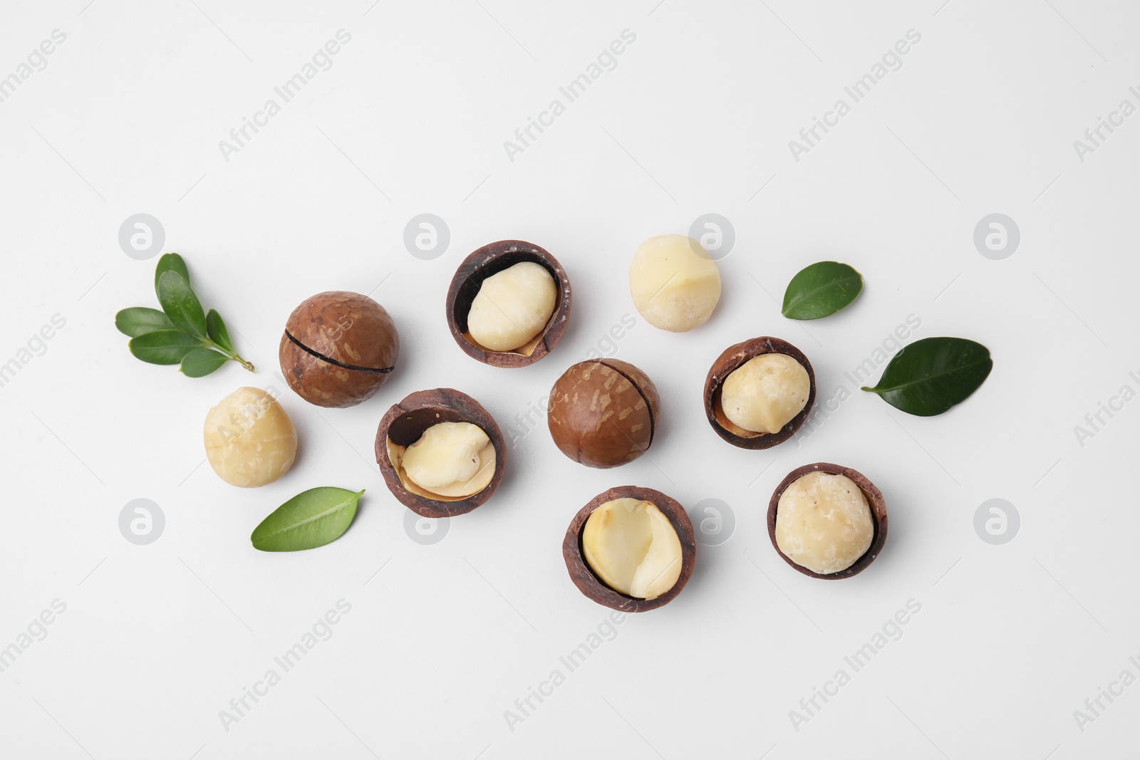 Photo of Tasty Macadamia nuts and green leaves on white background, flat lay