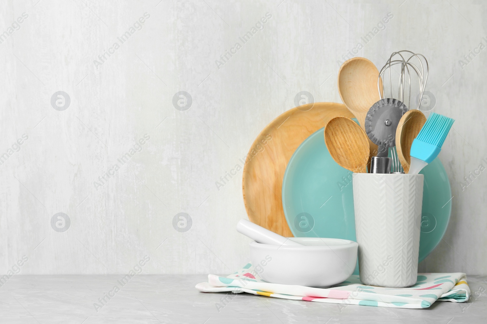 Photo of Different kitchen utensils on grey table against light background. Space for text