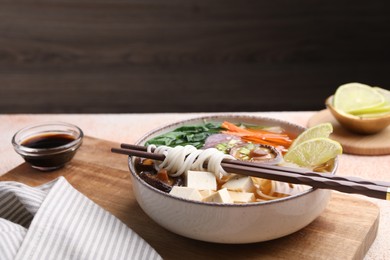Photo of Bowl of vegetarian ramen and chopsticks on light table, space for text
