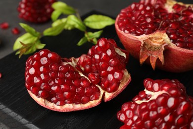 Photo of Cut fresh pomegranate and green leaves on table, closeup