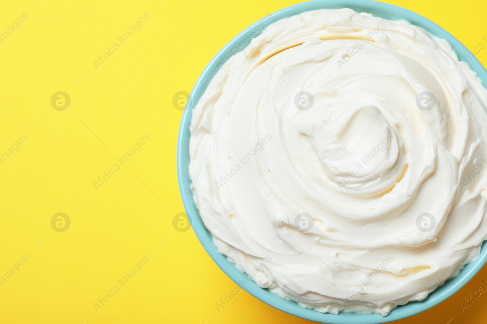 Photo of Bowl of tasty cream cheese on yellow background, top view. Space for text