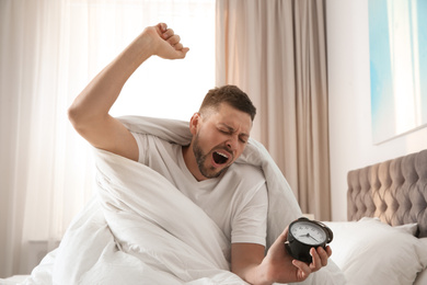 Photo of Sleepy man with alarm clock at home in morning