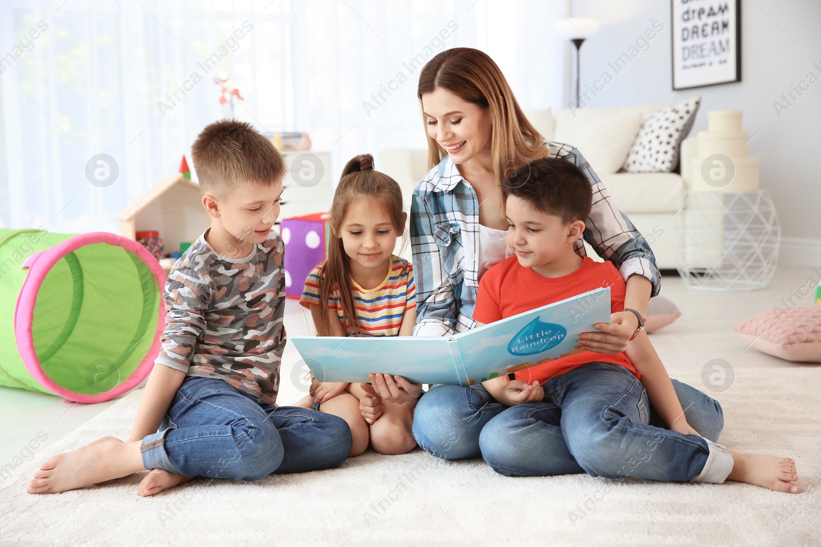 Photo of Cute little children reading book on floor with young mother in playing room