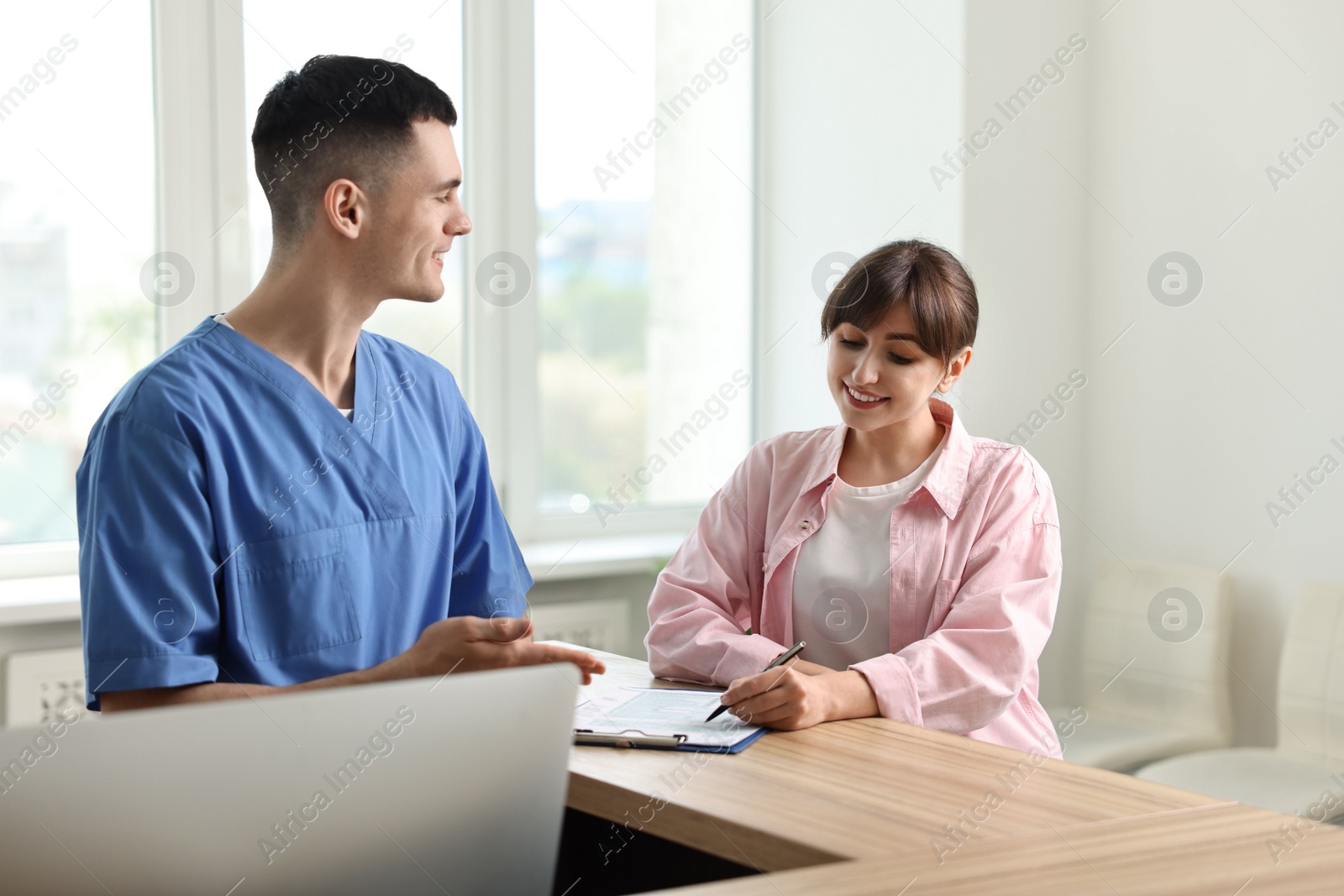 Photo of Smiling medical assistant working with patient at hospital reception