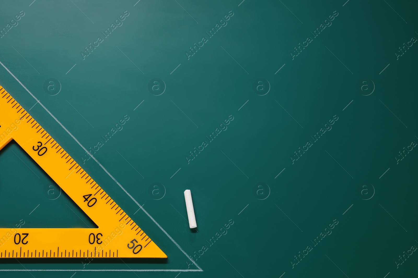 Photo of Yellow triangle and chalk on green chalkboard, flat lay. Space for text