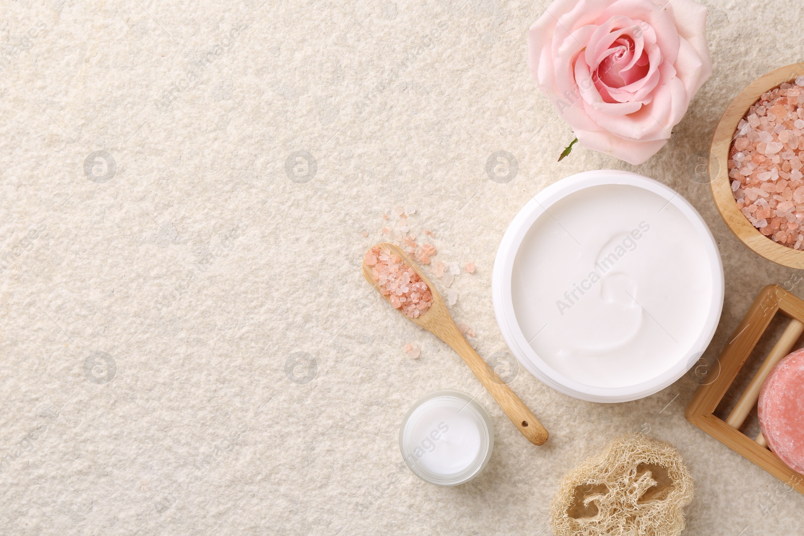 Photo of Flat lay composition with moisturizing cream in open jar and other body care products on light textured table. Space for text