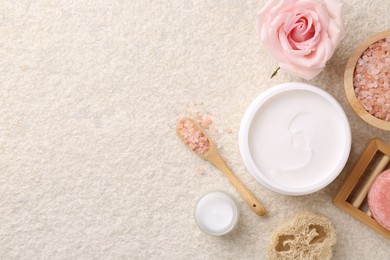 Flat lay composition with moisturizing cream in open jar and other body care products on light textured table. Space for text