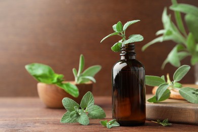 Photo of Bottle of essential oil and fresh herbs on wooden table, space for text