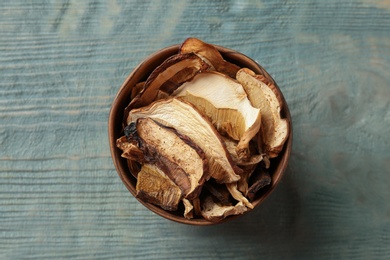 Photo of Bowl of dried mushrooms on color wooden background, top view