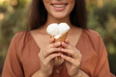 Photo of Young woman with delicious ice cream in waffle cone outdoors, closeup