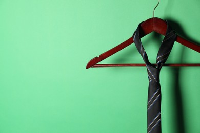 Hanger with black striped tie on green background. Space for text